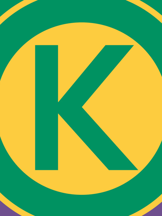 Eine grün-violette Flagge mit einem gelben Kreis in der Mitte. Der Kreis enthält einen fetten grünen Buchstaben „K“. Die Flagge hat einen gelben Rand, der das zentrale Motiv umgibt.