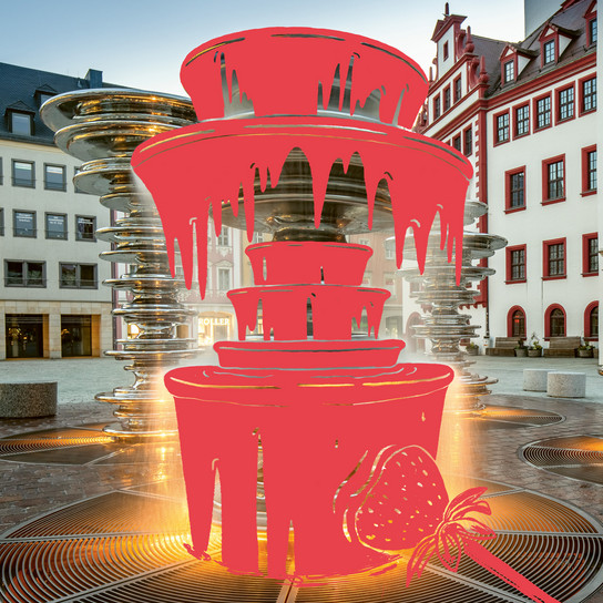 A digitally altered image of a city square with modern architecture, featuring a bright red overlay of a multi-tiered chocolate fountain and a strawberry illustration in the foreground.