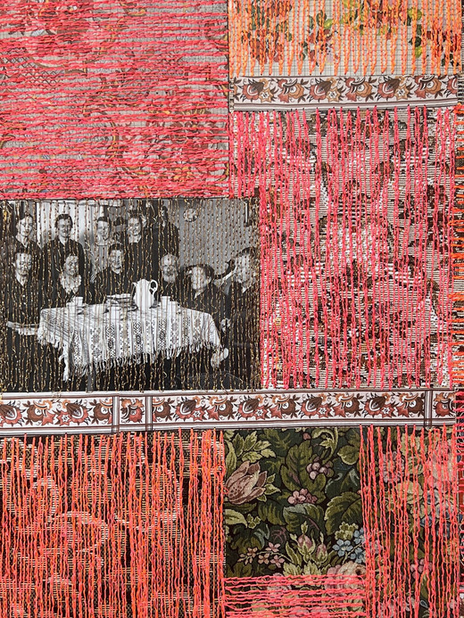 Ein Patchwork aus floralen und gemusterten Stoffquadraten, hauptsächlich in Rosa- und Orangetönen, mit vertikal herabhängenden orangefarbenen Fäden. Ein Quadrat enthält ein Schwarzweißfoto von Personen, die an einem Tisch sitzen.