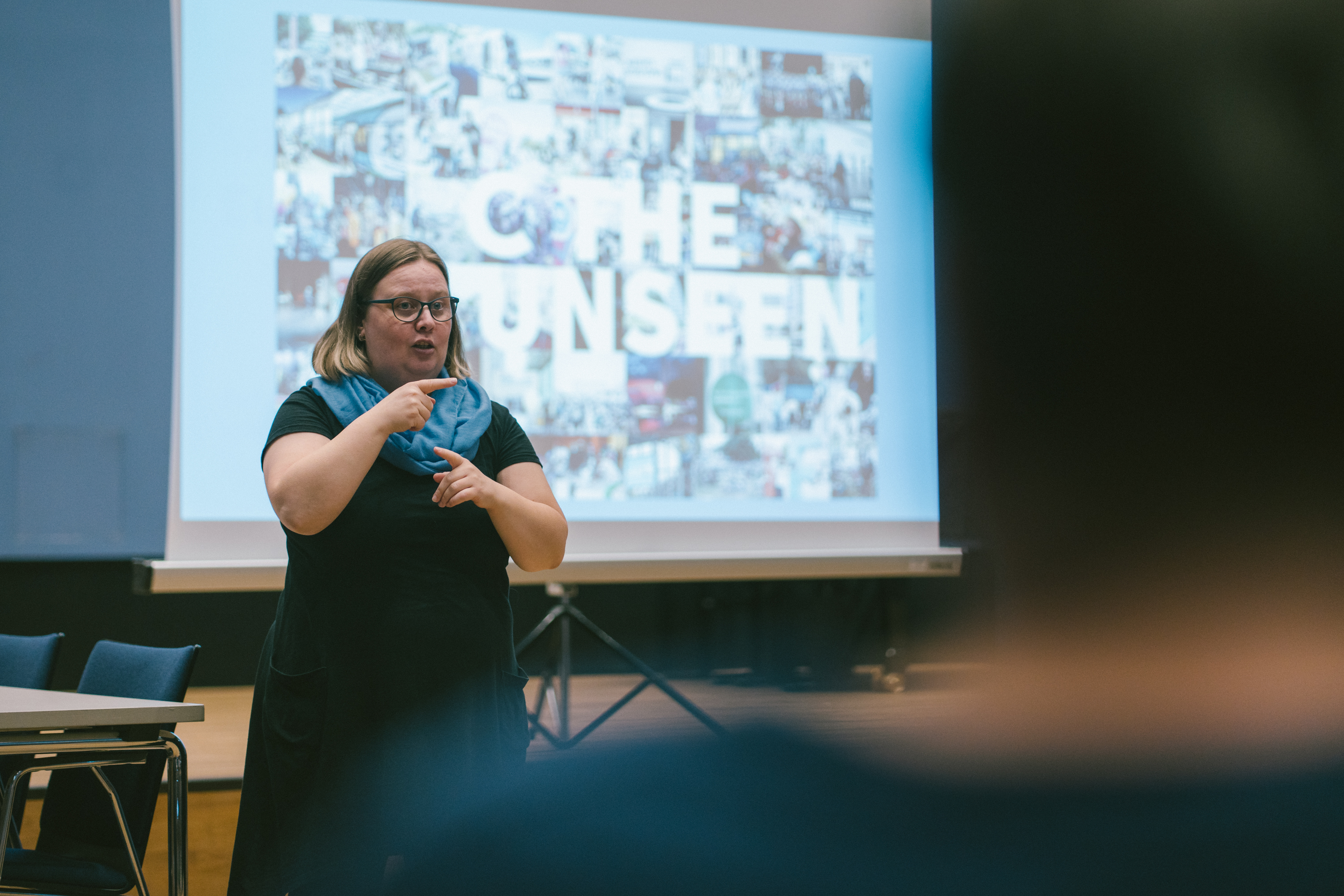 Eine Frau steht vor einer Leinwand und übersetzt in deutsche Gebärdensprache.